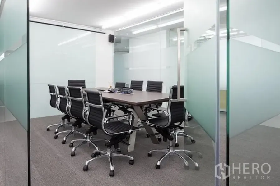 Office Space for rent in Khlong Toei, Bangkok - Modern conference room with glass partitions, long wooden table and black swivel chairs on carpet flooring.