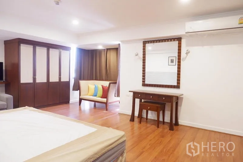 Condominium for rent in Khlong Toei, Bangkok - Spacious bedroom with wardrobe, dressing table and window seating with colorful cushions.