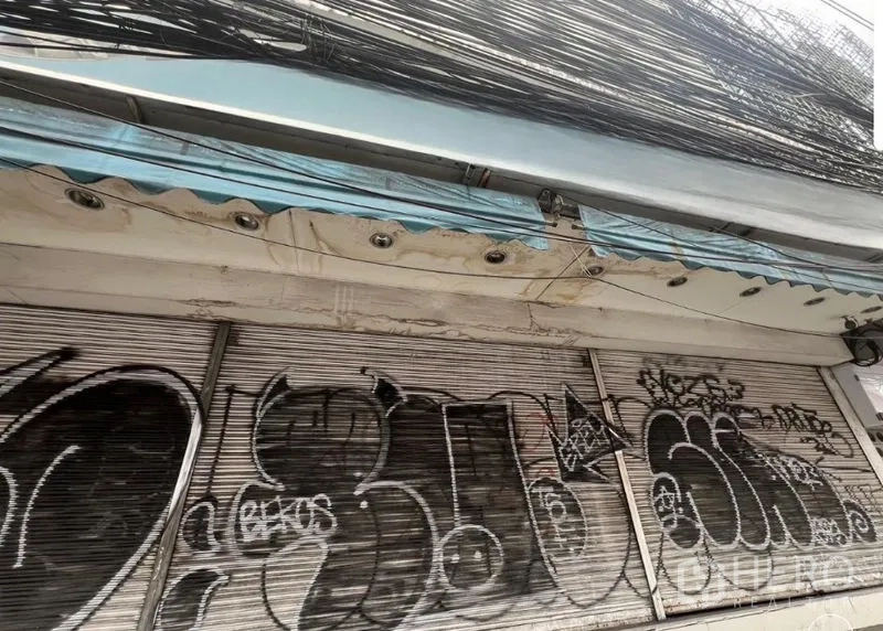 店屋 出租在Watthana, Bangkok - 临街店屋外观，卷帘门关闭并有涂鸦，带雨棚与密集的空中电缆。