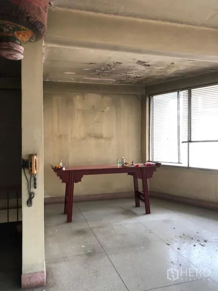 店屋 出租在Bangkok - 室内空置空间，混凝土天花与旧墙面，靠大窗摆放一张木桌。