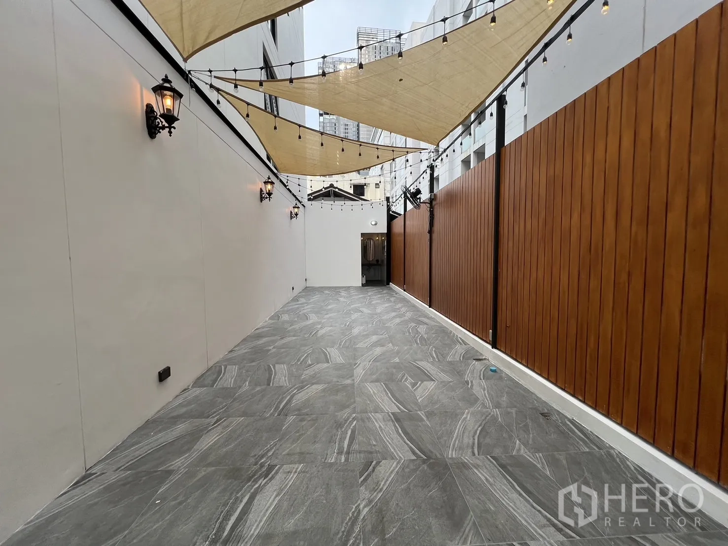 Retail Space for rent - Long outdoor walkway with lantern wall lights, wood privacy fence and canopy sails with string lights.