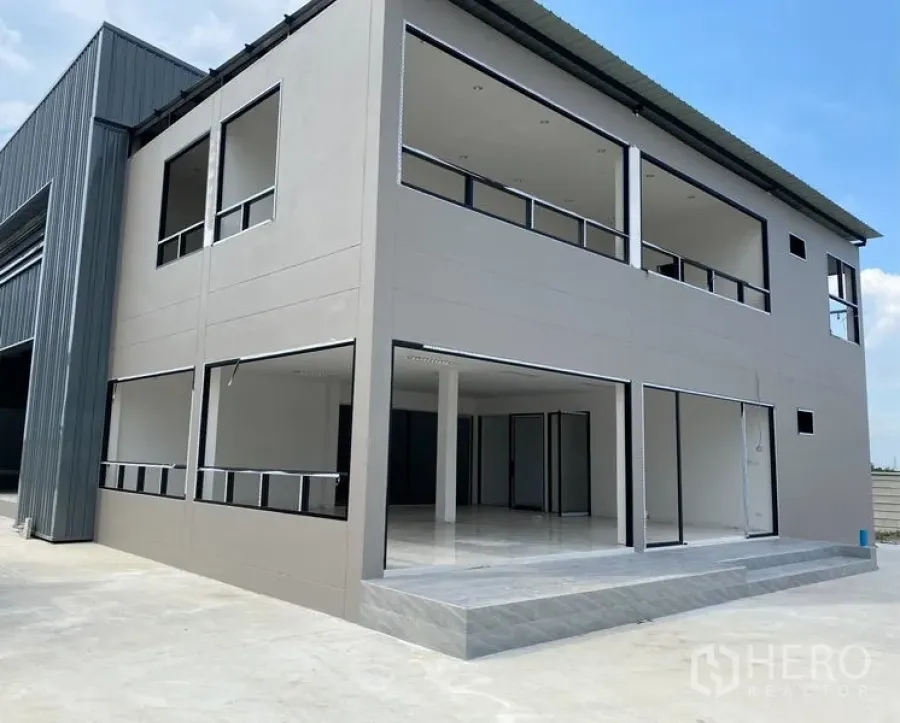 Warehouse for rent or sale in Bang Len, Nakhon Pathom - Modern two-storey office building attached to the warehouse with wide driveway and parking apron.