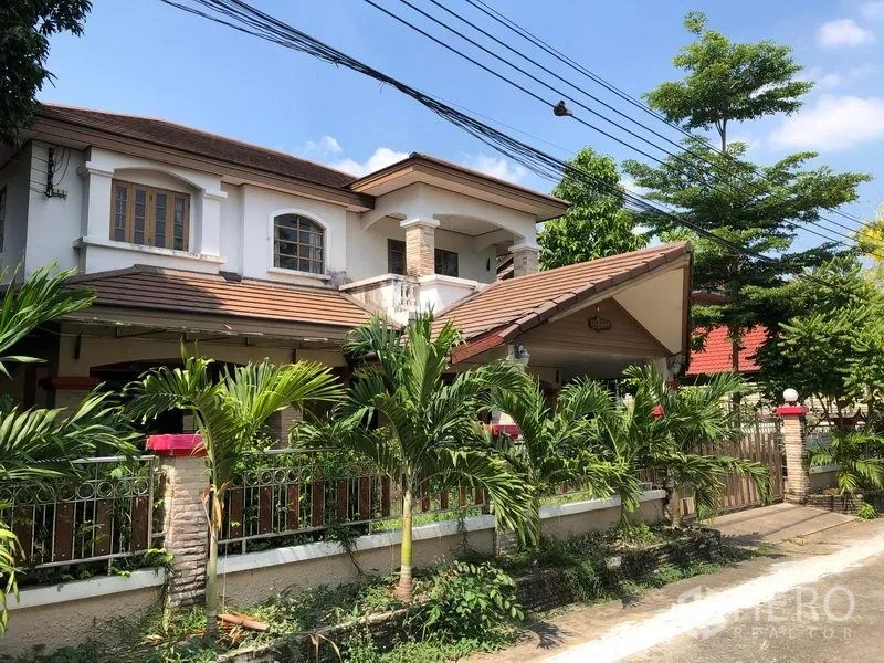 บ้าน ขายในPak Kret, Nonthaburi - มุมมองด้านข้างบ้านเดี่ยว ปากเกร็ด มีที่จอดรถมีหลังคา เสาแต่งหิน รั้วเหล็ก และสวนทรอปิคอลตามแนวกำแพง