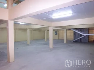 Factory for rent in Thung Khru, Bangkok - Spacious production area with columns, a metal staircase, and folding metal doors.