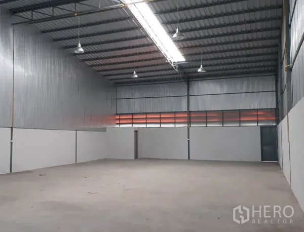 Warehouse for rent in Mueang Pathum Thani, Pathum Thani - Spacious high-ceiling warehouse interior with corrugated metal walls, skylight strip lighting, and smooth concrete floor in Pathum Thani.