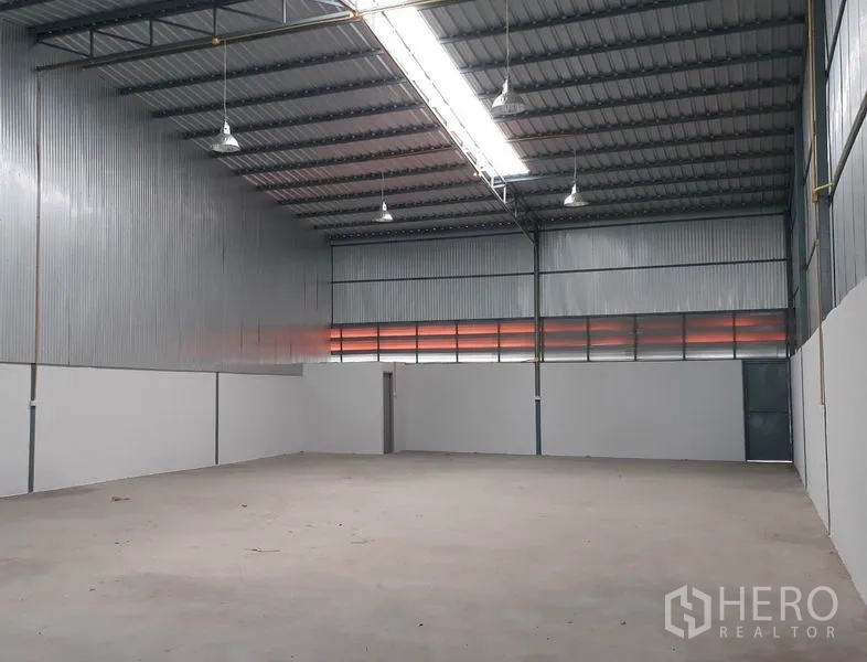 Warehouse for rent in Mueang Pathum Thani, Pathum Thani - Spacious high-ceiling warehouse interior with corrugated metal walls, skylight strip lighting, and smooth concrete floor in Pathum Thani.