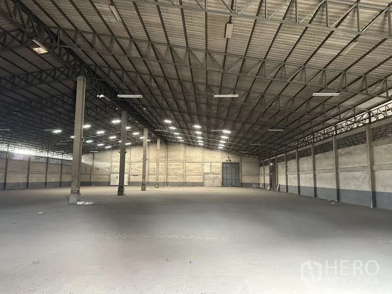 Warehouse for rent in Pak Kret, Nonthaburi - Wide warehouse floor with multiple columns, metal roof and rear loading doors.