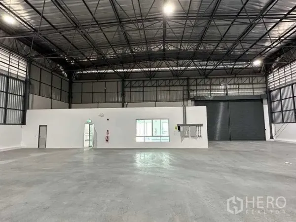 Factory for rent in Bang Sao Thong, Samut Prakan - Spacious warehouse interior featuring a high steel truss roof, polished concrete floor and a roller shutter.