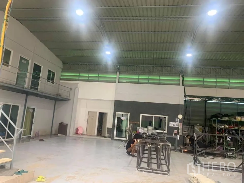 Warehouse for sale in Lam Luk Ka, Pathum Thani - Spacious warehouse interior with high ceiling, mezzanine offices, and bright LED lighting.