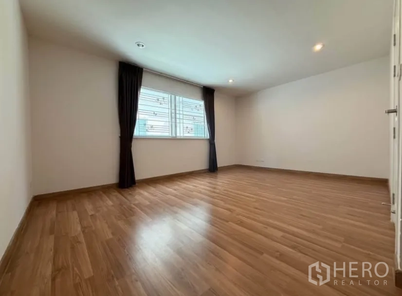 Townhouse for rent in Suan Luang, Bangkok - Sunlit bedroom with wide window, curtains and wood floors.