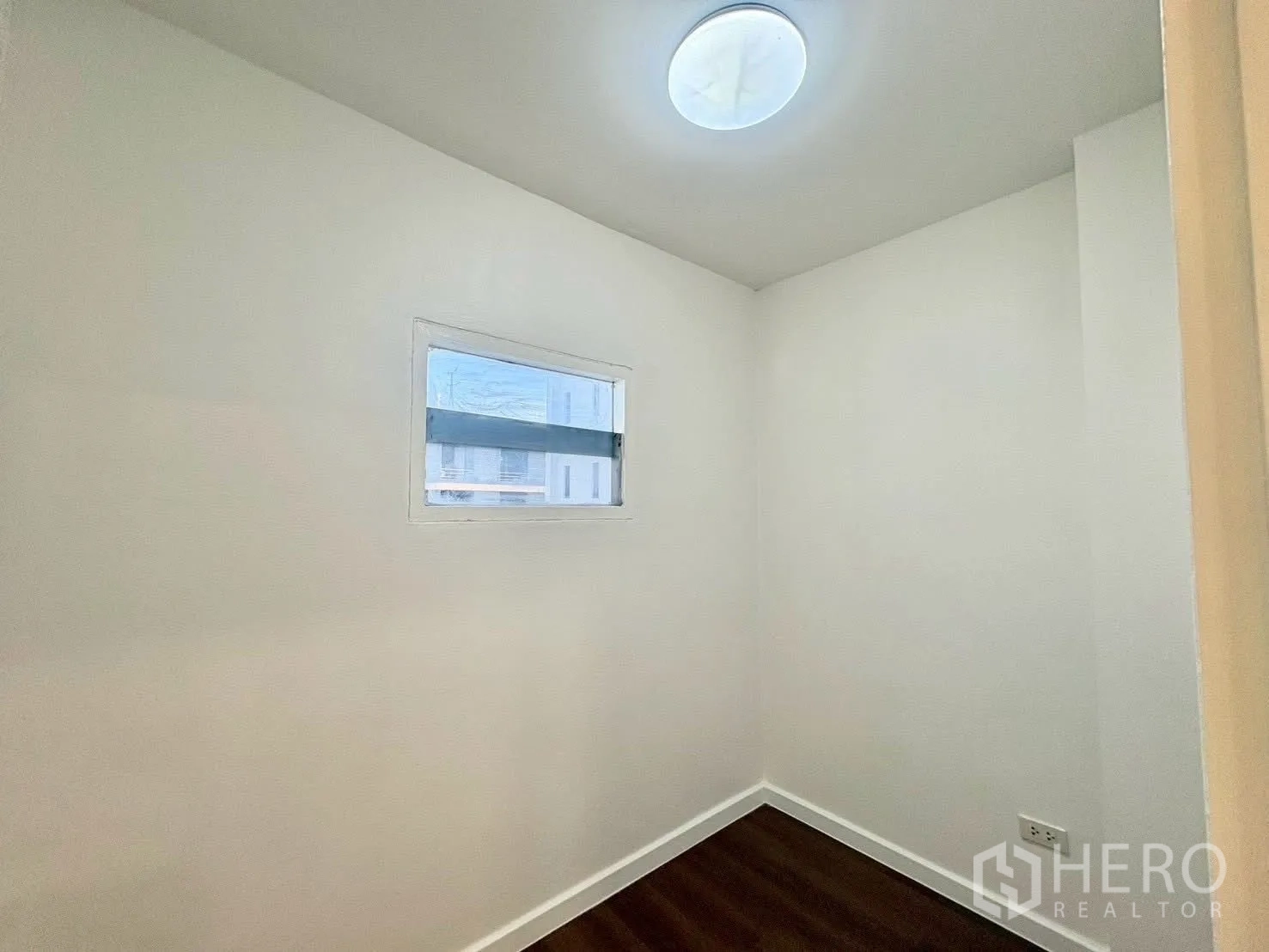 Townhouse for rent in Huai Khwang, Bangkok - Compact room with white walls, wood flooring, and a narrow window.