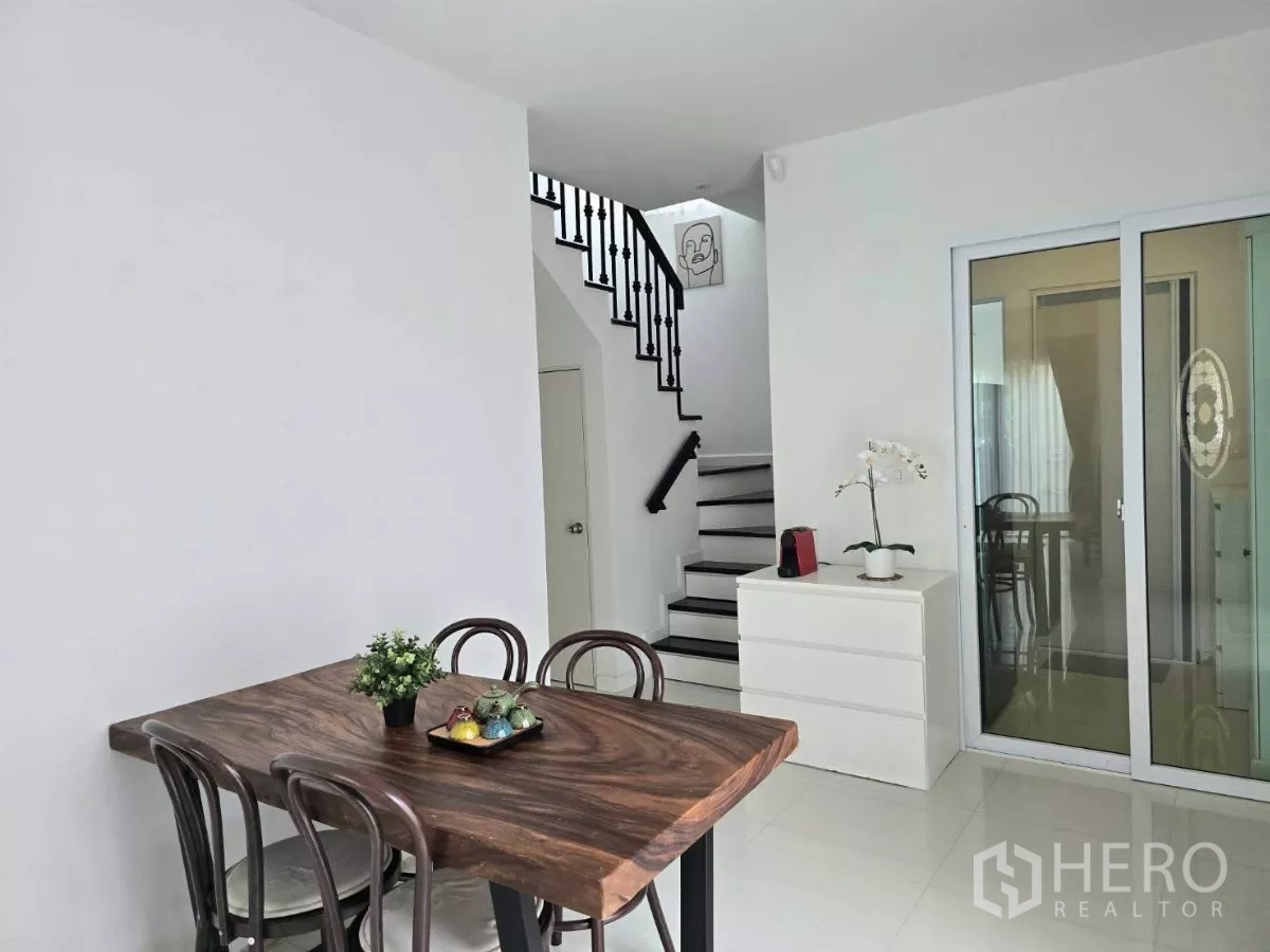 Detached House for rent in Samut Prakan - Dining area with solid wood table, staircase and sliding doors to the patio.
