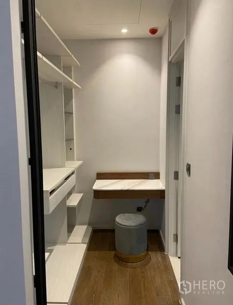 Condominium for rent in Pathum Wan, Bangkok - Compact walk-in closet with built-in shelves, mirror, and small vanity desk with stool.