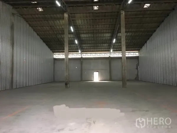 Warehouse for rent in Bang Phli, Samut Prakan - Wide clear-span warehouse hall with central columns, illuminated ceiling and a rear access door.