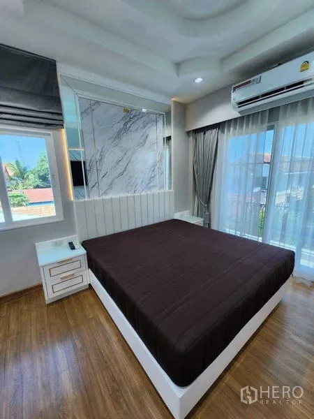 Detached House for rent in Bang Khen, Bangkok - Master bedroom with large bed, marble accent headboard, wood flooring and balcony doors.