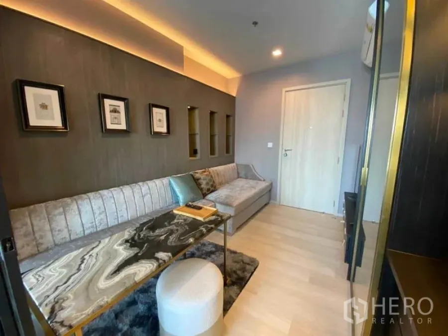 Condominium for rent in Pathum Wan, Bangkok - Cozy living space with cove lighting, framed wall niches and a stone-pattern table.