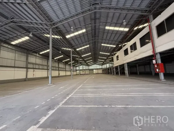 Factory for rent in Lat Krabang, Bangkok - Wide open warehouse bay under metal roof with skylight panels, fire-safety piping and mezzanine offices on the right.