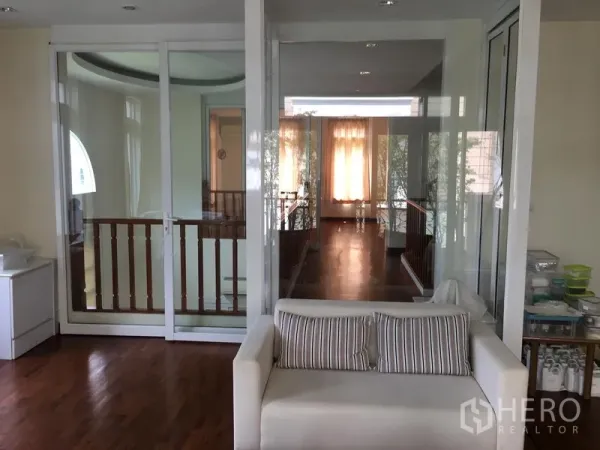 Townhouse for sale in Huai Khwang, Bangkok - Hallway and sitting area separated by full-height glass doors and a wooden stair balustrade.