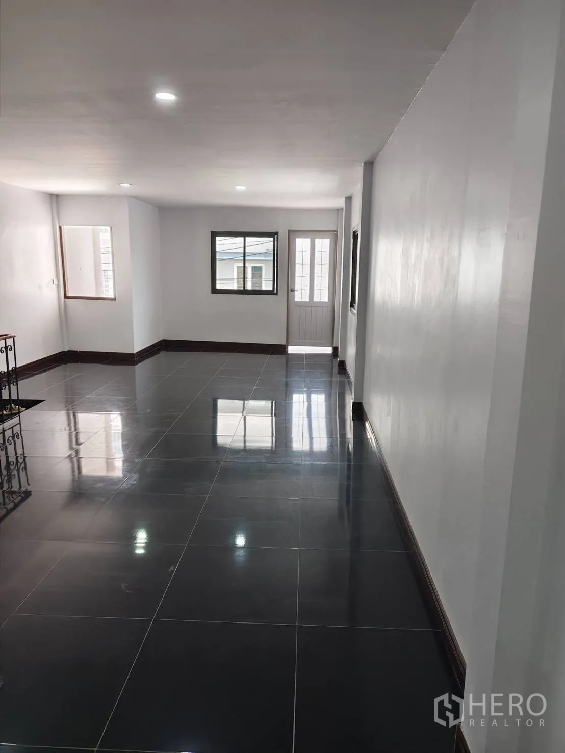 Townhouse for sale in Phra Khanong, Bangkok - Bright upstairs space with windows and a balcony door over polished black tiles.