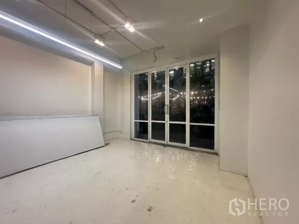Home Office for rent in Pathum Wan, Bangkok - Bright workspace with long LED strip lighting and full-height glass doors facing greenery.