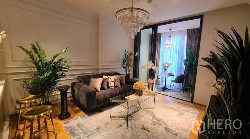 Condominium for rent in Khlong Toei, Bangkok - Stylish living room with wall paneling, plush sofa, indoor greenery and a chandelier above a modern rug.