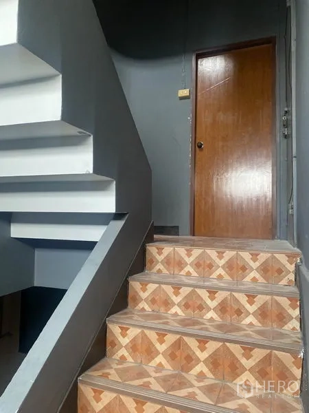 Shophouse for rent in Watthana, Bangkok - Stairwell with patterned tile steps and a wooden door against gray walls