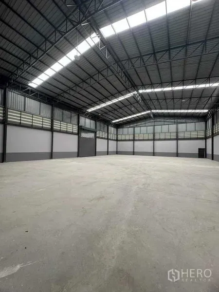 Factory for sale in Samut Sakhon - Spacious high-ceiling warehouse with steel trusses, skylights and smooth concrete floor.
