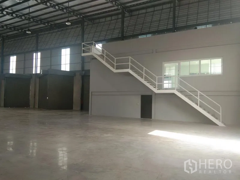 Warehouse for rent in Bang Phli, Samut Prakan - Internal mezzanine office with white staircase overlooking the warehouse and several roller doors along the wall.