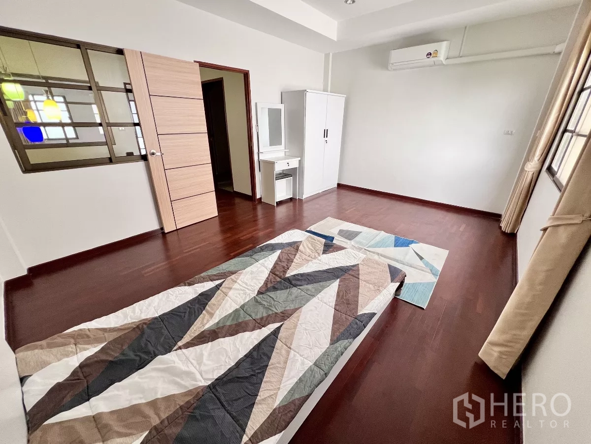 Townhouse for rent or sale in Phra Khanong, Bangkok - Spacious bedroom with wood flooring, air conditioning, and a large window.