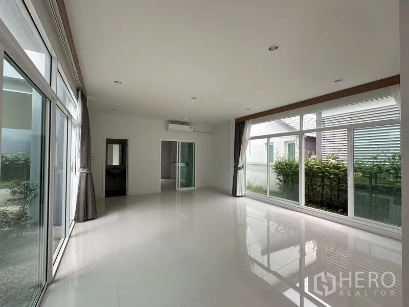Detached House for sale in Lam Luk Ka, Pathum Thani - Family room view with wraparound windows overlooking hedges.