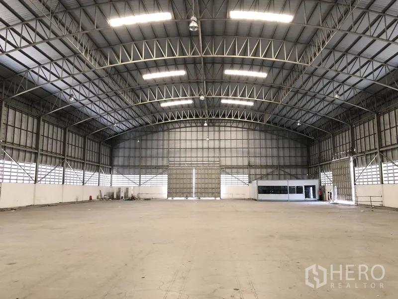 Warehouse for rent in Pathum Thani - Bright open warehouse hall with illuminated steel rafters, roller doors and an internal office box.