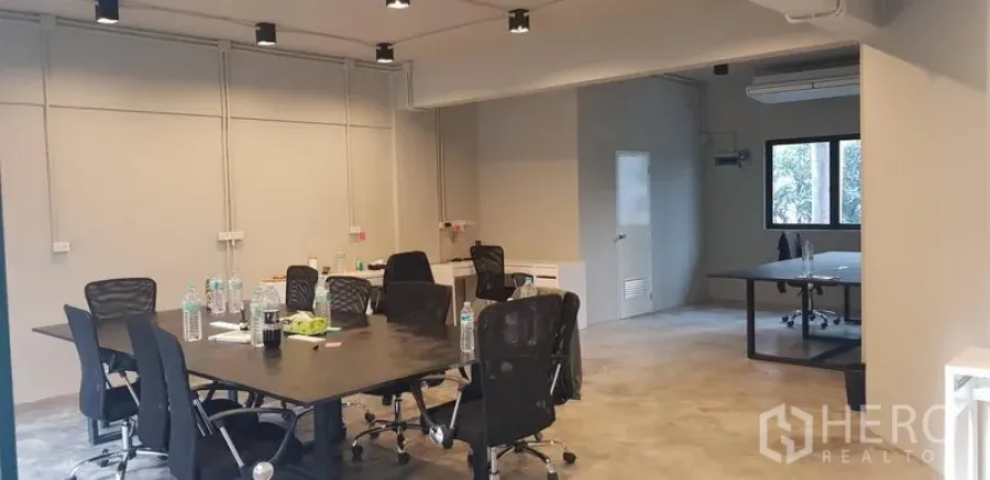 Office Space for rent in Khlong Toei, Bangkok - Wide view of modern workspace with track lighting, multiple desks and an adjoining room with window and AC.