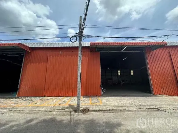 Warehouse for rent in Bang Kapi, Bangkok - Front view of a warehouse with sliding doors, wide awning, marked loading zones and overhead power lines.