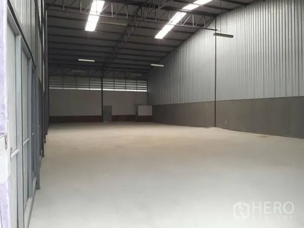 Warehouse for rent in Lam Luk Ka, Pathum Thani - Spacious high-ceiling warehouse interior with concrete floor, steel trusses, and skylight panels.