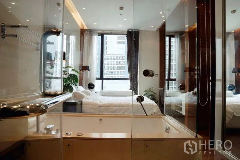 Condominium for rent in Khlong Toei, Bangkok - Glass‑walled bathroom with bathtub and shower, looking into the bedroom and city outside.