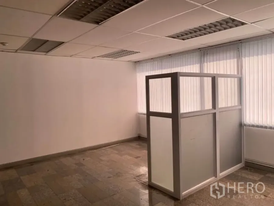 Office Space for rent in Khlong Toei, Bangkok - Corner office interior with vertical blinds, suspended ceiling lights and a frosted glass partition on stone-tile flooring.
