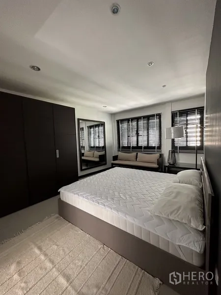 Condominium for rent in Khlong Toei, Bangkok - Spacious bedroom with king bed, wardrobe, window bench, and blinds.