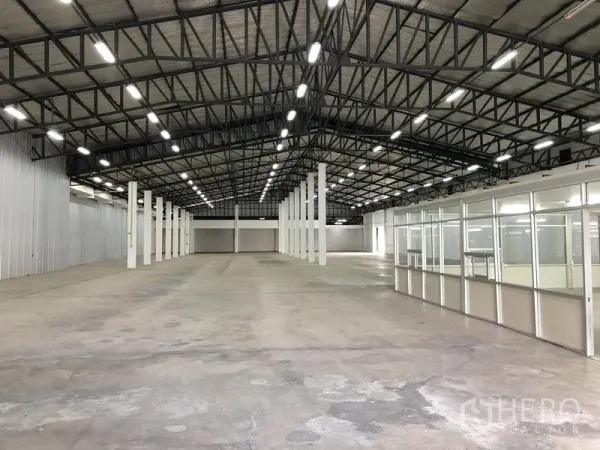 Warehouse for rent in Nonthaburi - Wide warehouse floor with a metal-clad side wall and an office block along the right.