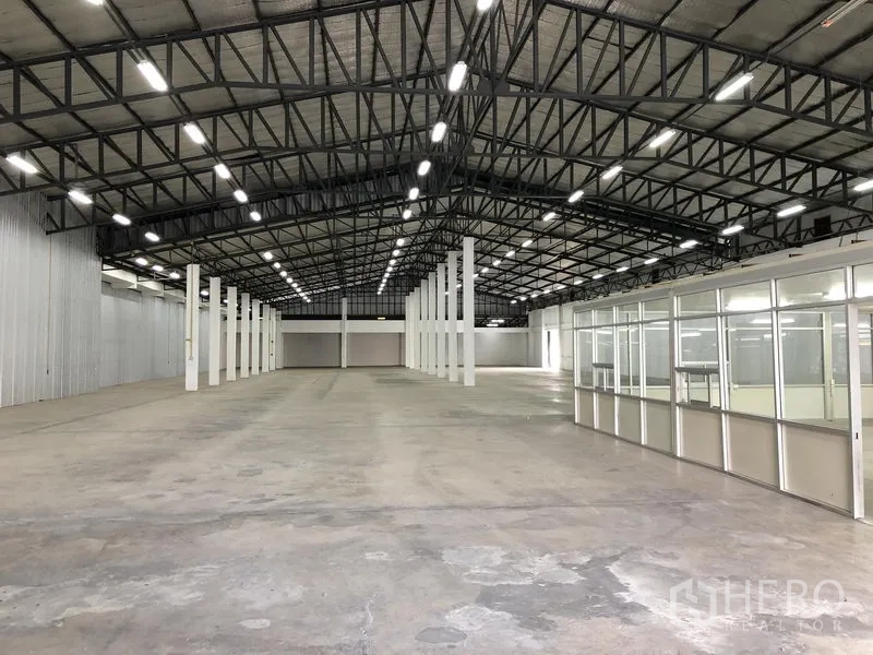 Warehouse for rent in Nonthaburi - Wide warehouse floor with a metal-clad side wall and an office block along the right.