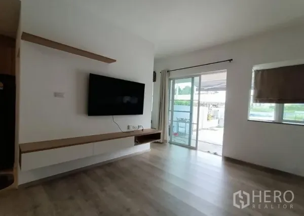 Townhouse for rent in Prawet, Bangkok - Bright living room with wall-mounted TV, floating shelf and sliding glass doors to the patio.