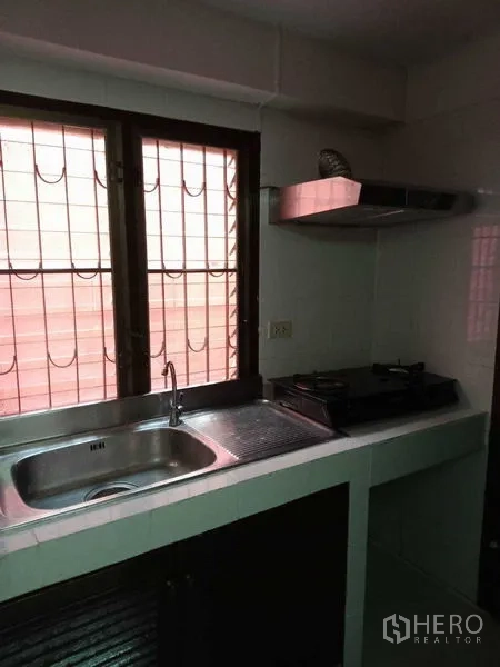 Townhouse for rent in Khlong Toei, Bangkok - Prep area with sink, gas hob, and window with security grilles.