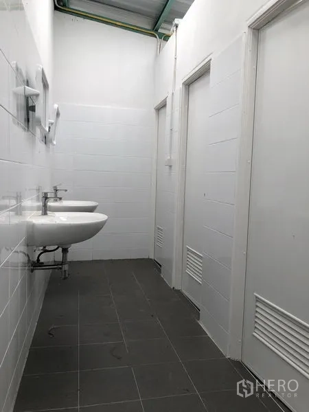 Factory for rent or sale in Bang Phli, Samut Prakan - Clean white-tiled washroom corridor with twin basins and cubicle doors.