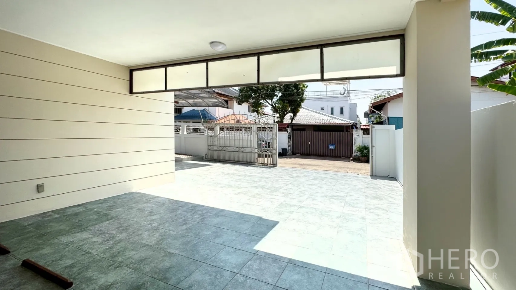 บ้านเดี่ยว for rent in Suan Luang, Bangkok - ที่จอดรถในร่มมองออกไปยังประตูรั้วเหล็กบานเลื่อนและลานหน้าบ้านปูกระเบื้องกว้าง