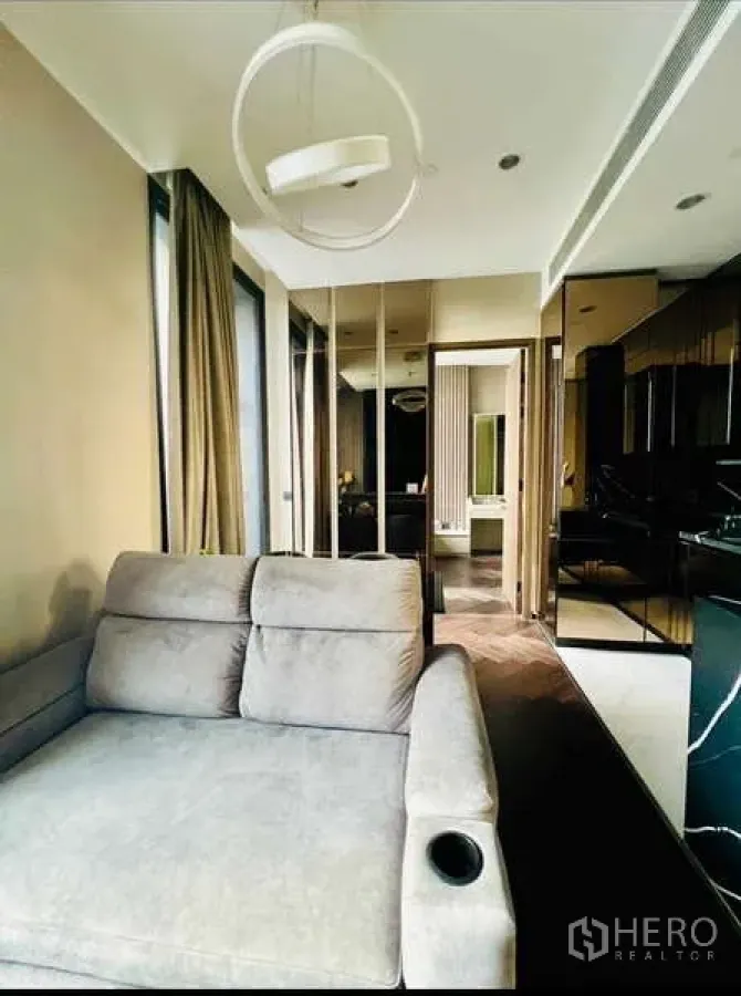 Condominium for rent in Khlong Toei, Bangkok - Open‑plan lounge adjoining sleek kitchenette with dark cabinets, wood flooring and full‑height curtains.