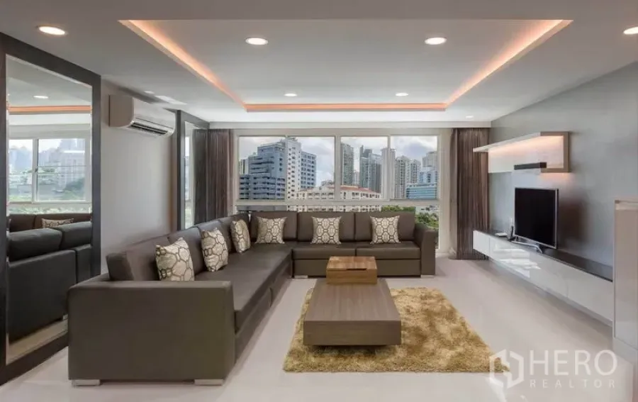 Condominium for rent in Khlong Toei, Bangkok - Living room with L‑shaped sofa, TV console and wide windows framing the Bangkok skyline.