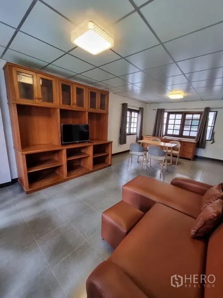 Detached House for rent in Nonthaburi - Lounge with sectional sofa, TV cabinet, and a dining set by the windows.