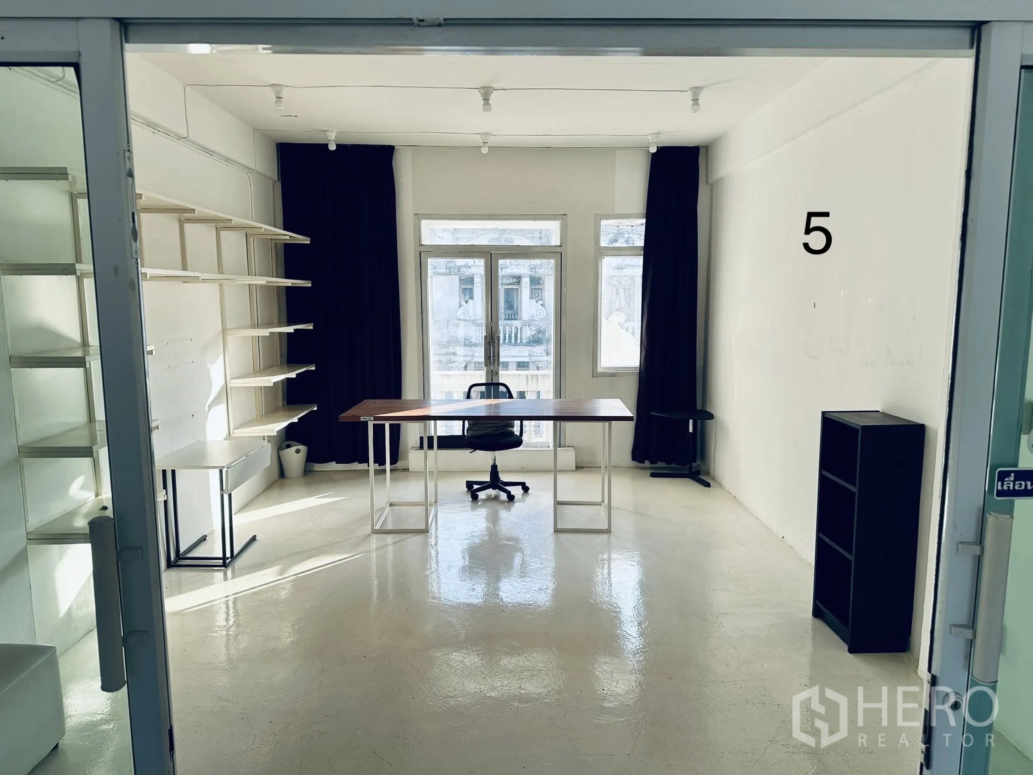 Shophouse for rent in Watthana, Bangkok - Glass-partitioned workspace with desk, chair, wall shelving, and windows with dark curtains.