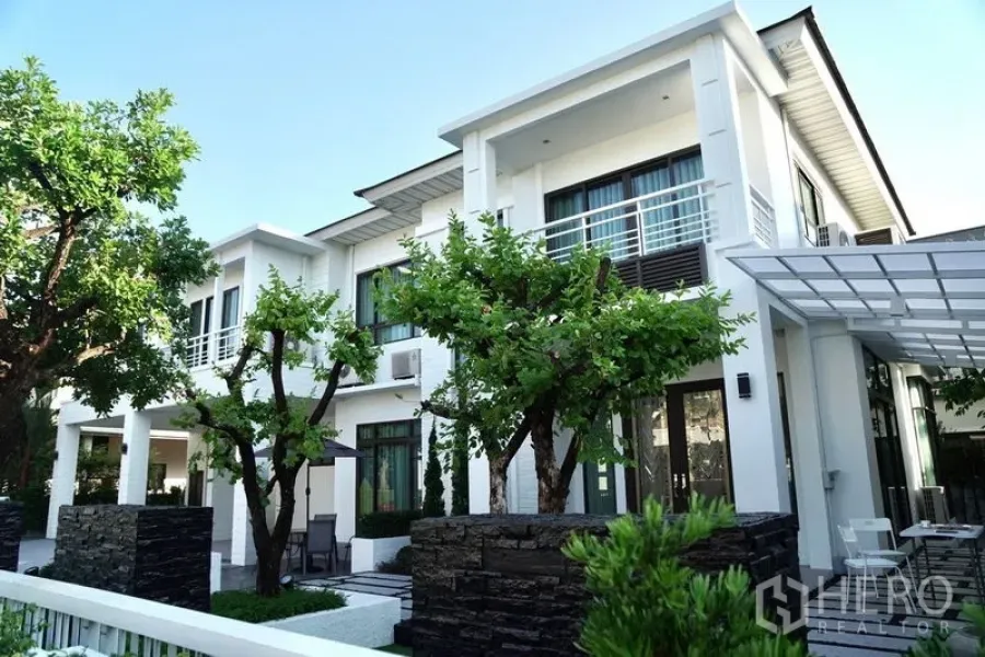 Detached House for rent - Daytime exterior of a contemporary white two-storey house with balconies and garden trees.
