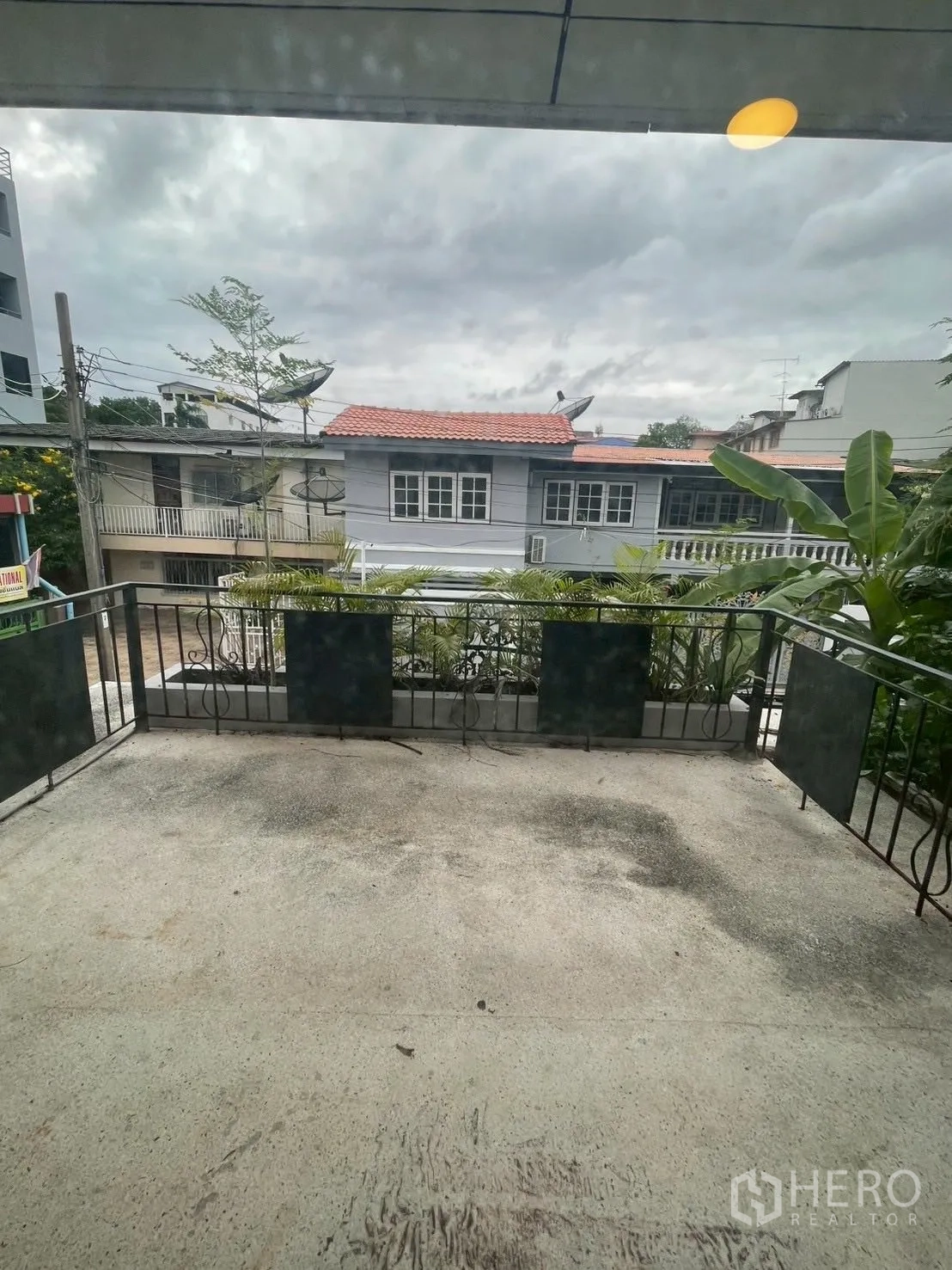 Detached House for rent in Watthana, Bangkok - Spacious balcony with metal railing overlooking neighborhood houses under a cloudy sky.