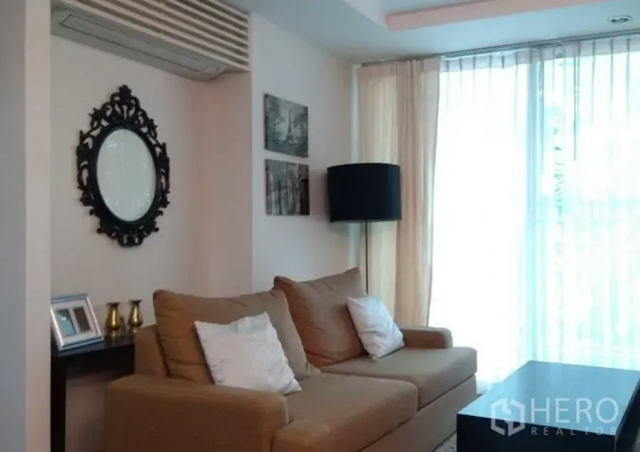 Condominium for rent in Khlong Toei, Bangkok - Bright living room with beige sofa, coffee table, sheer floor-to-ceiling curtains and a black floor lamp.